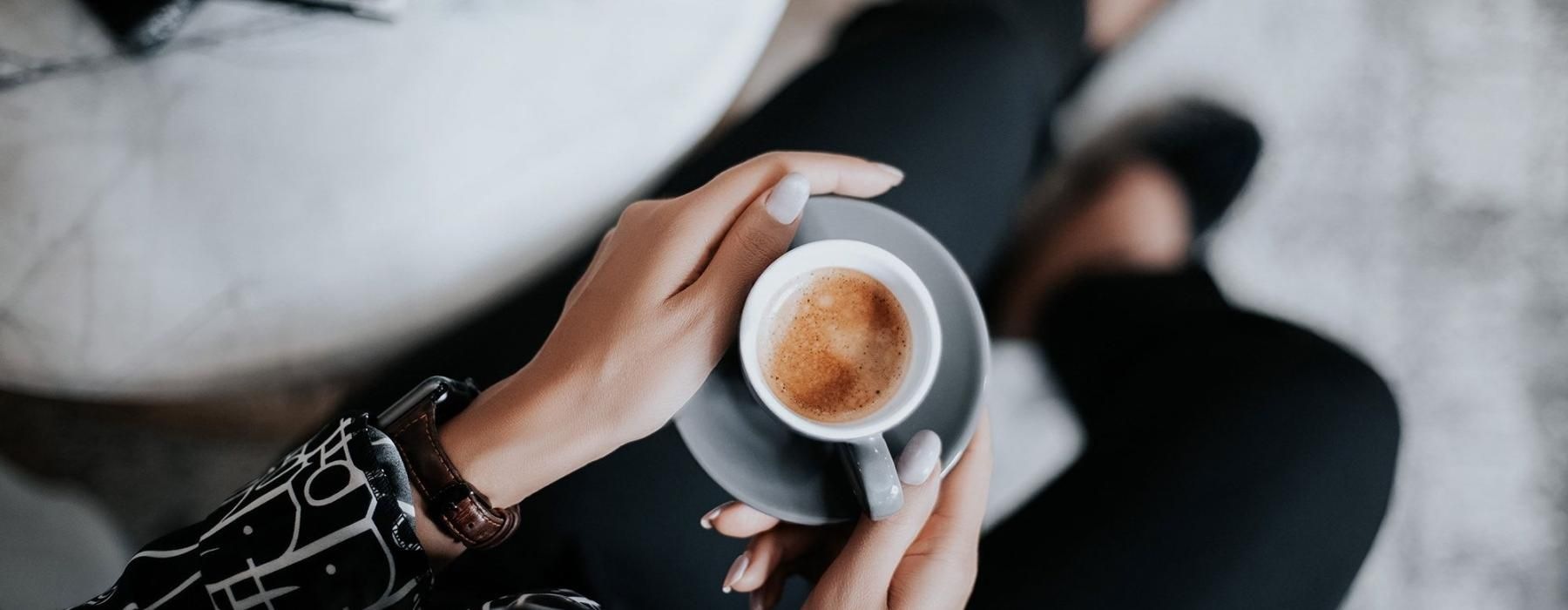 business woman sits next to a marble table with books and holds a saucer with a cup of espresso